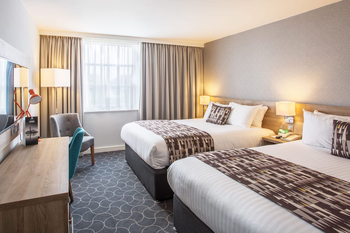 A hotel room with two beds, a desk, a chair, and a TV.