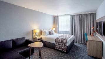 A hotel room with a bed, a desk, a chair, a TV, and a window with curtains.