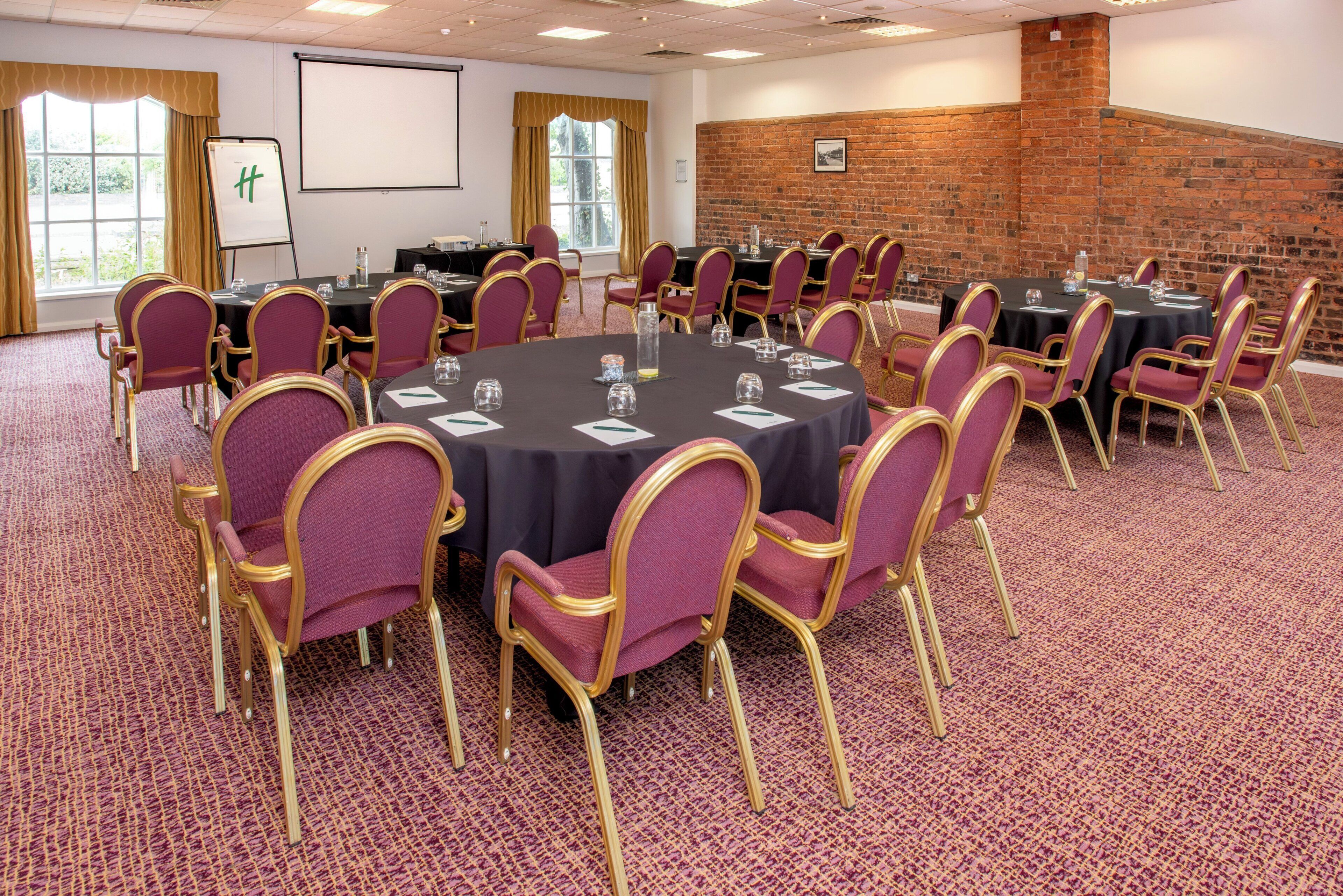 A conference room with round tables, chairs, a projector screen, and a brick wall.