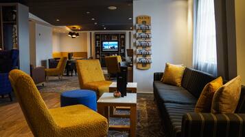 A hotel lobby with a sofa, chairs, a TV, and a wall with magazines.