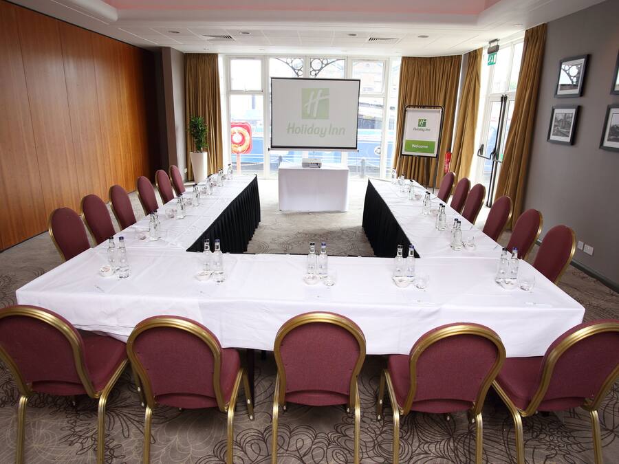 A conference room with a long table set for a meeting, surrounded by chairs, a screen, and framed pictures on the walls.