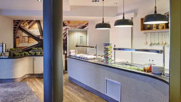 A modern kitchen area with a counter, hanging lights, and a tiled backsplash.