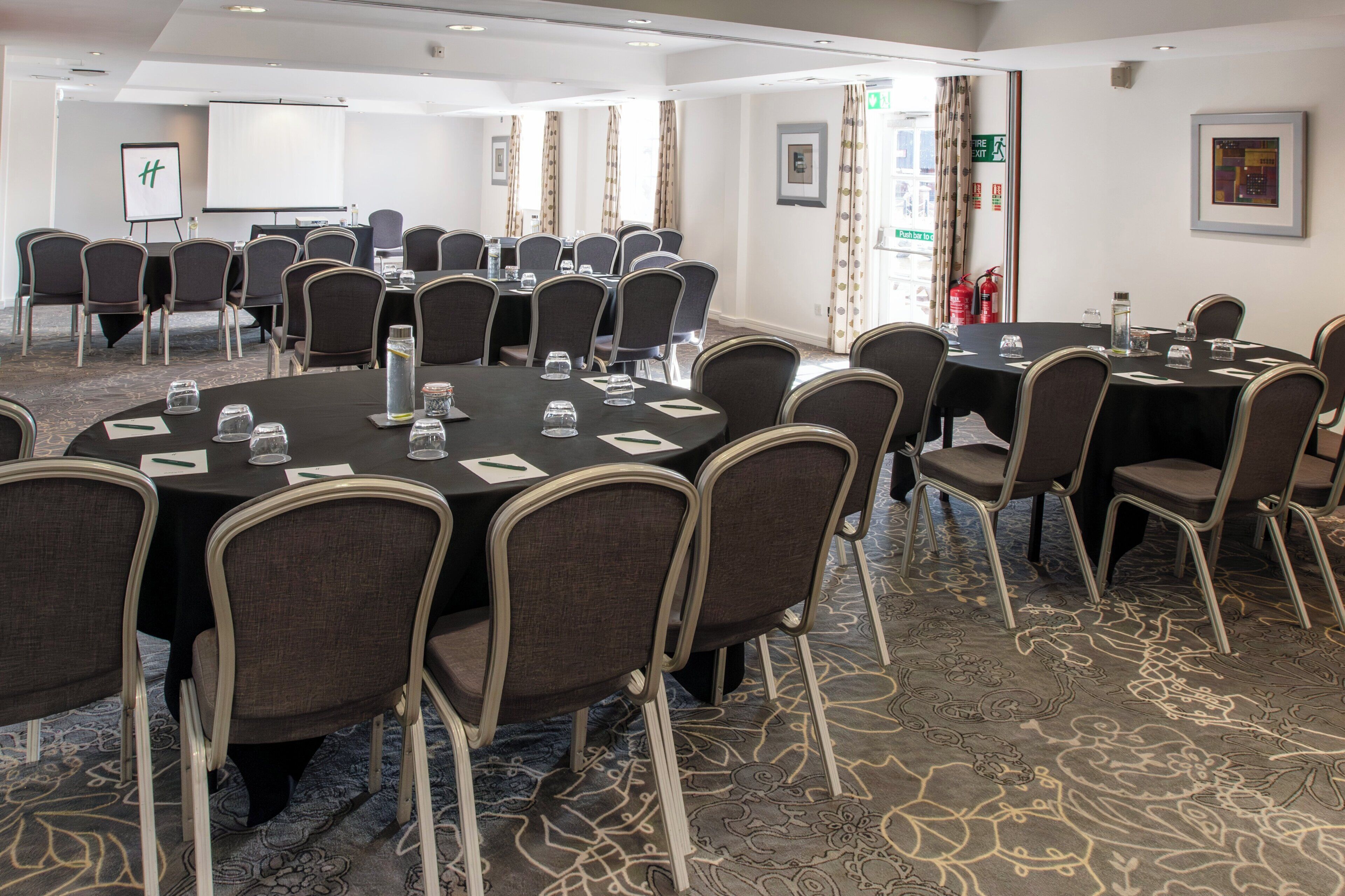 A conference room with round tables, chairs, and a projector screen.