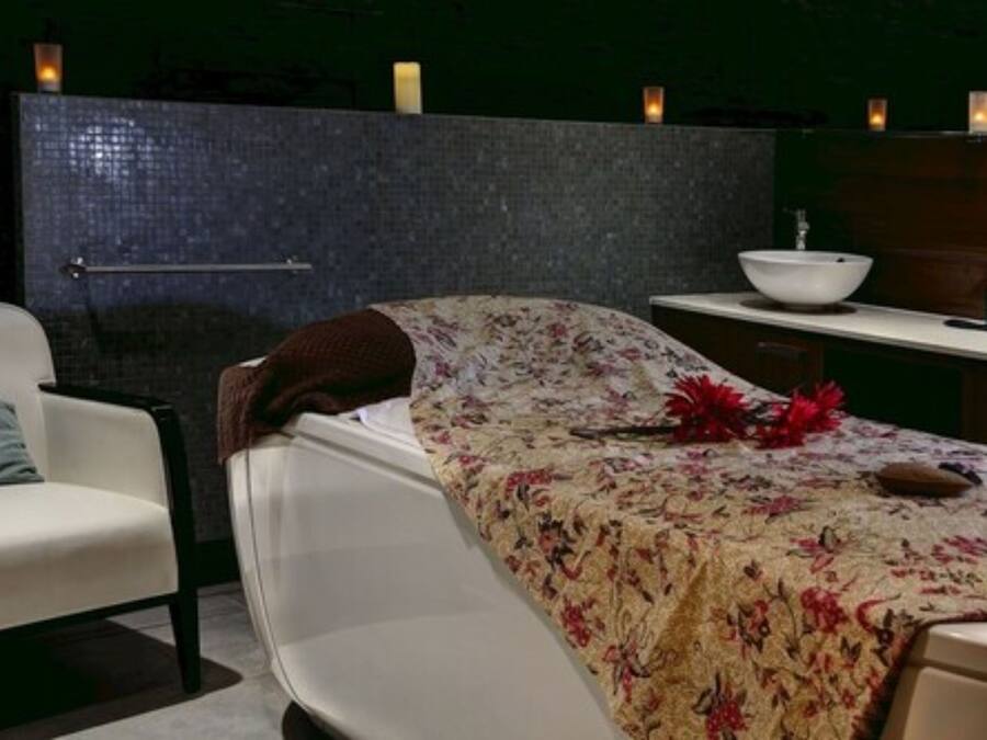 A spa room with a bed, a white chair, a wooden cabinet, and a large mirror.