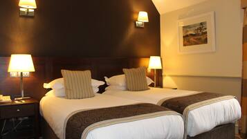 A double bed with two pillows, a nightstand with a lamp, and a wall-mounted picture.