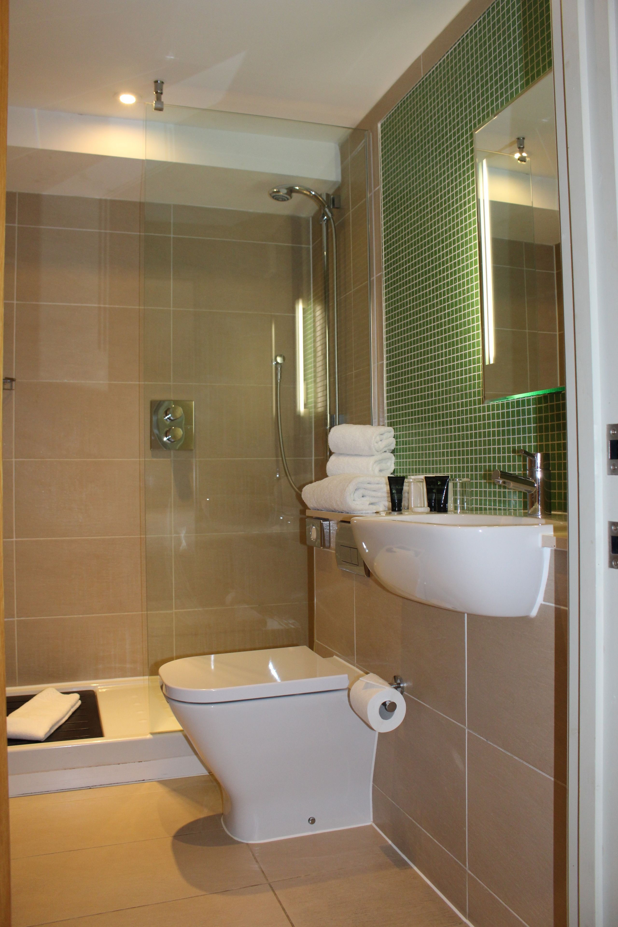 A bathroom with a shower, toilet, sink, and a green-tiled wall.