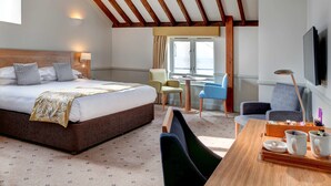 Une chambre d’hôtel avec un grand lit, un bureau sur lequel se trouve un plateau avec divers objets, et un téléviseur fixé au mur.
