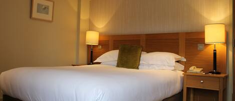 A hotel room with a large bed, two bedside tables with lamps, a wooden headboard, and a framed picture on the wall.