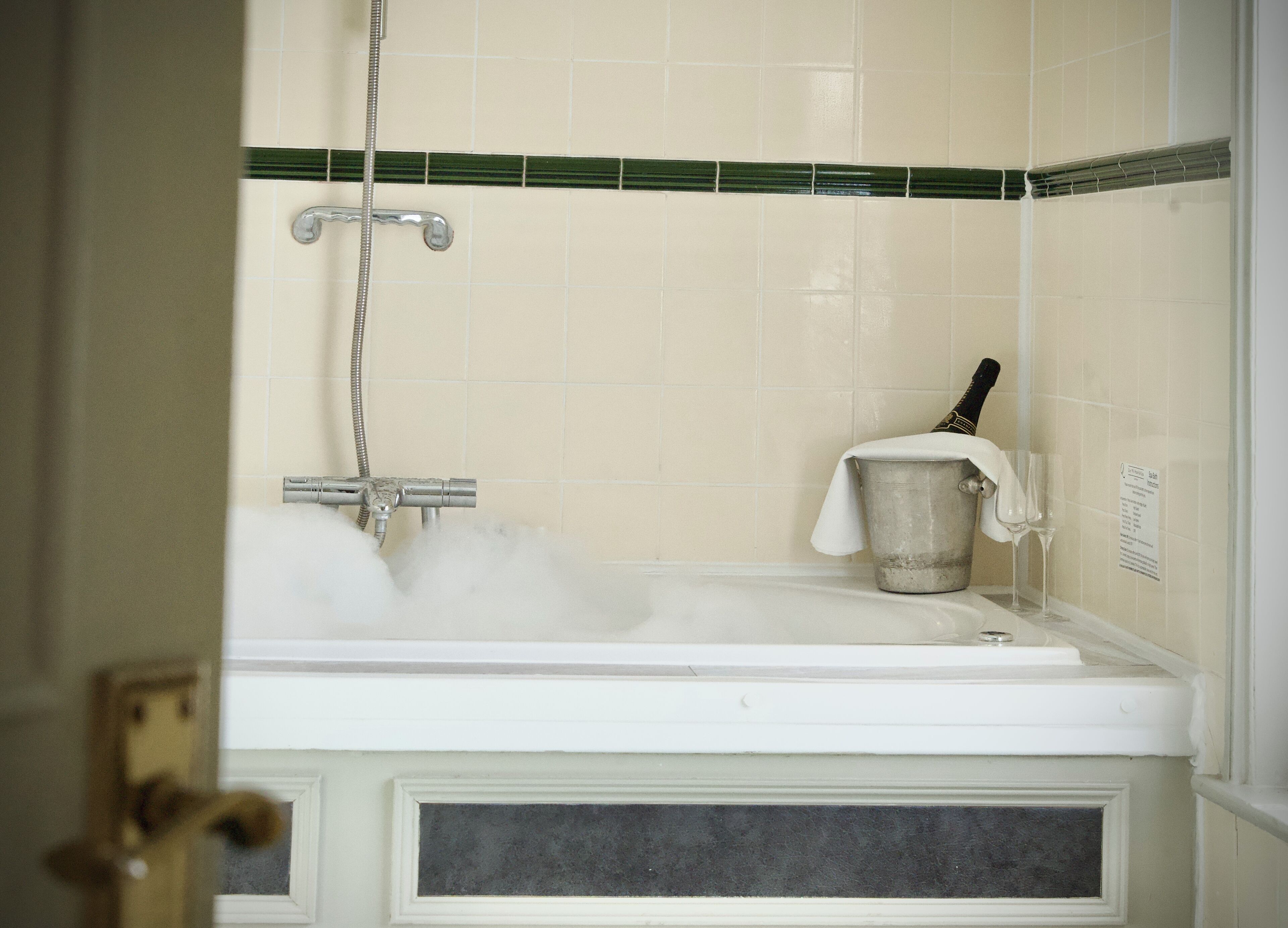 A bathroom with a bathtub filled with water, a showerhead, and a towel hanging on a hook.