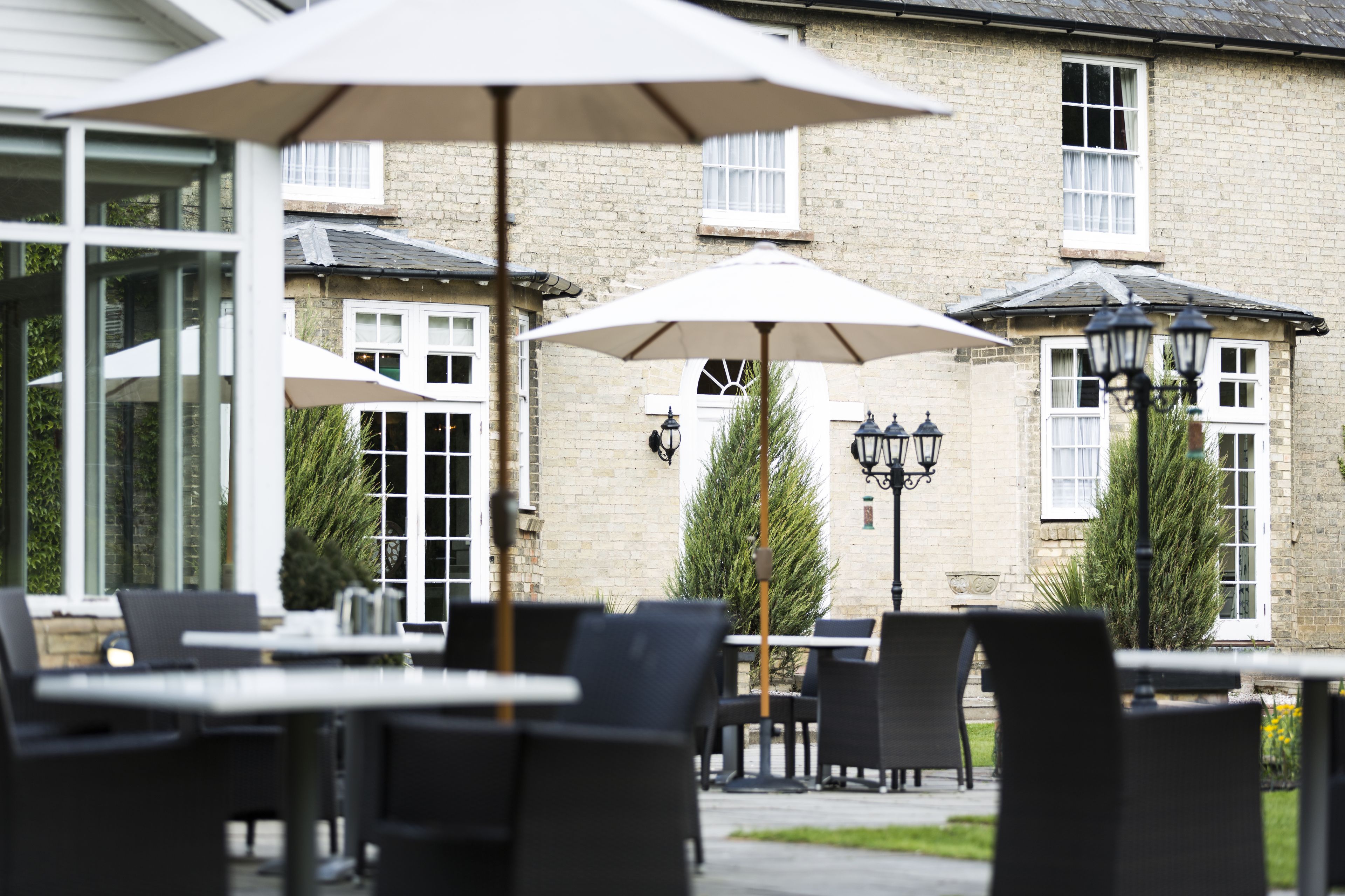 An outdoor seating area with tables and chairs, umbrellas, and a stone building with windows in the background.