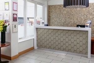 A reception area with a white counter, a tiled floor, a decorative wall, and framed certificates on the wall.