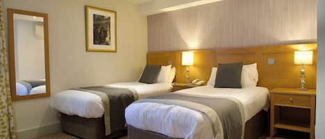 Une chambre d’hôtel avec deux lits, une table de chevet avec une lampe, un miroir et un tableau encadré au mur.