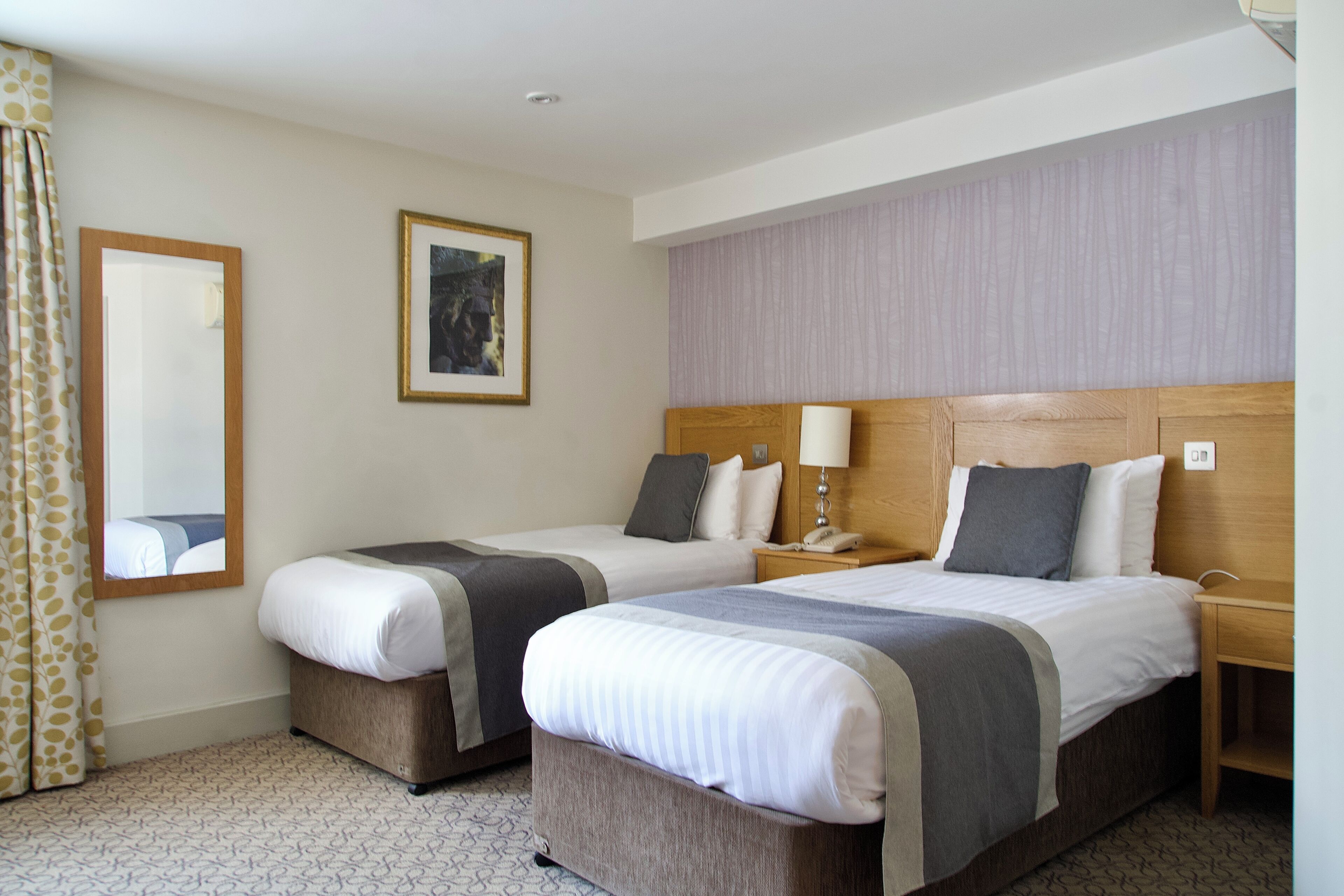 A hotel room with two beds, a mirror, a framed picture, and a patterned carpet.