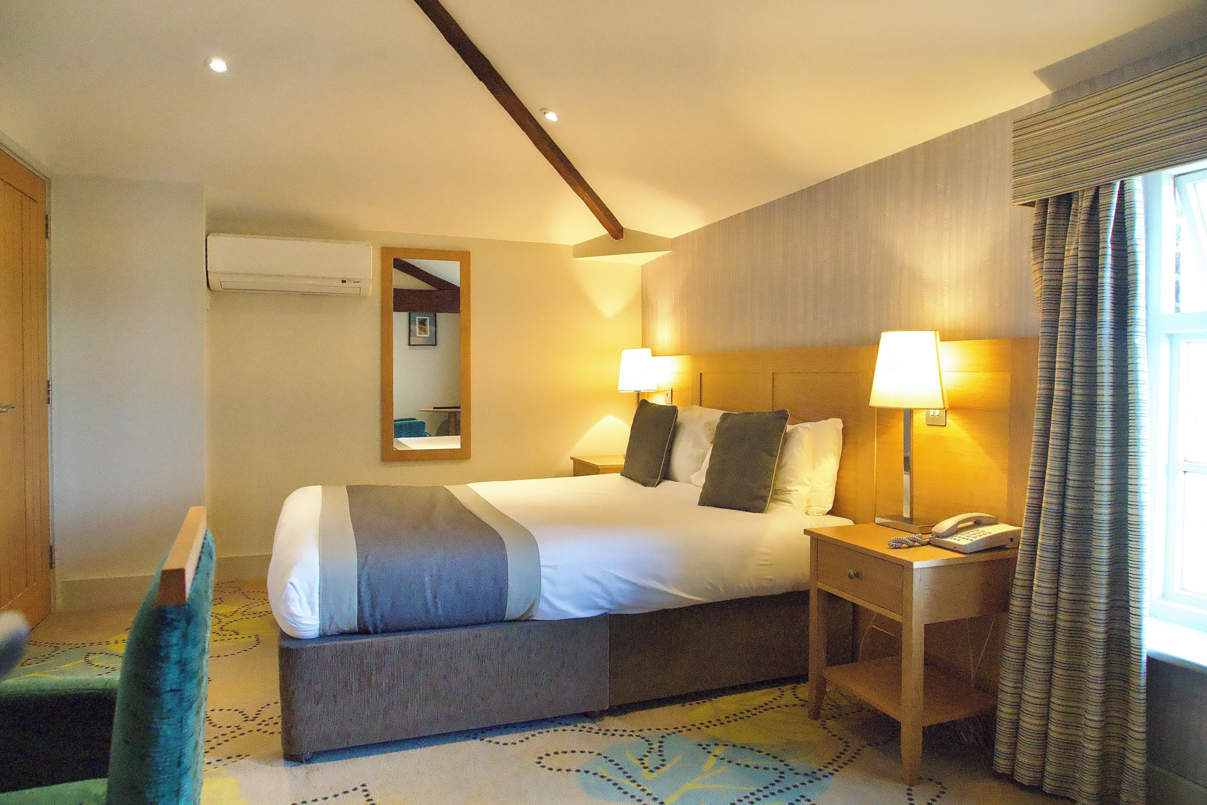 A hotel room with a bed, bedside lamps, a telephone, and a window with curtains.