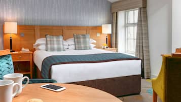 Habitación de hotel con una cama grande, dos mesitas de noche, una mesa redonda con un teléfono inteligente, dos tazas y una silla.