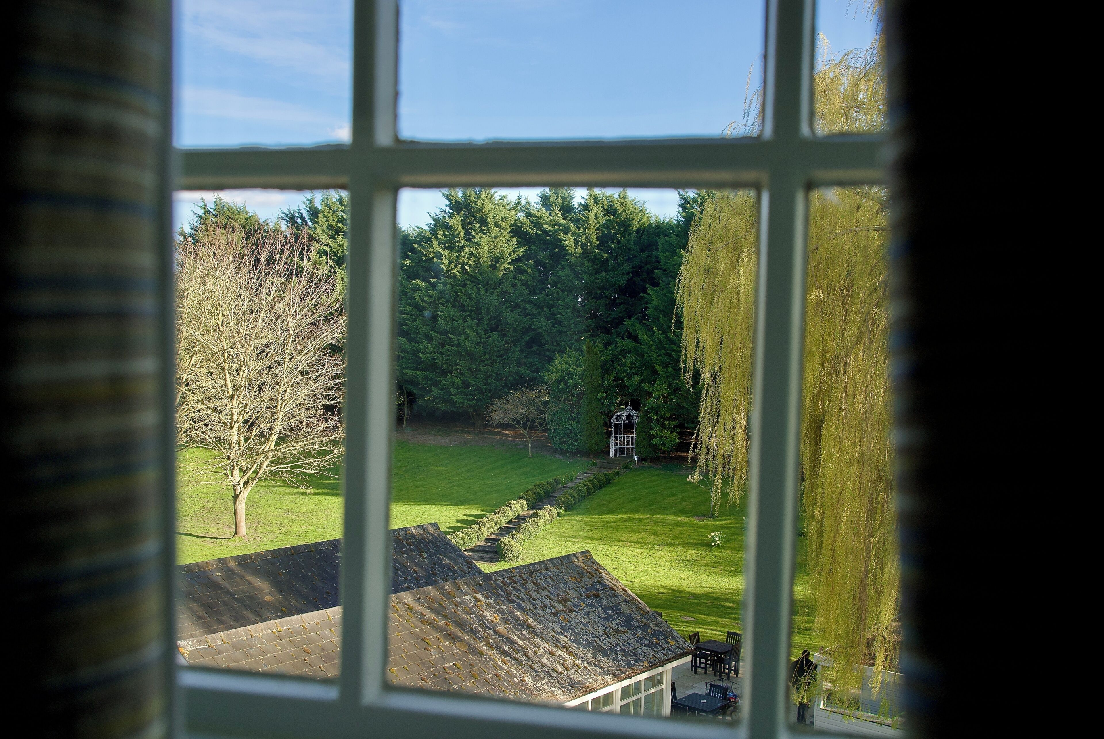 A view through a window of a house with a lawn, a gazebo, and a tree.