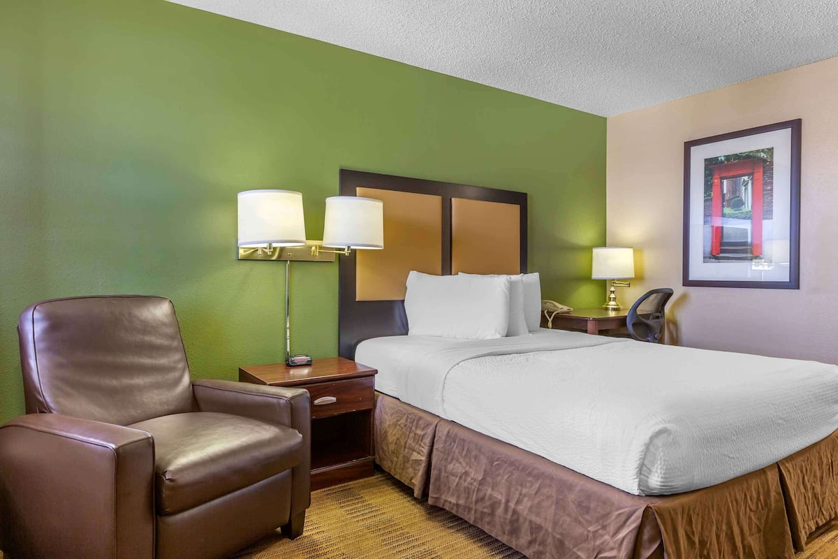 Una habitación de hotel con una cama, una silla, una mesita de noche y una lámpara.