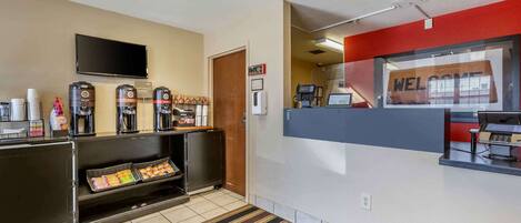 A hotel reception area with a flat-screen TV, coffee machines, and a welcome sign.
