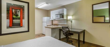 A hotel room with a bed, a desk with a chair, a microwave, and a refrigerator.