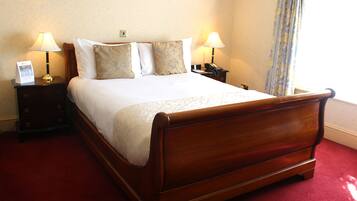 A neatly made bed with a wooden frame, two bedside tables with lamps, and a red carpeted floor.