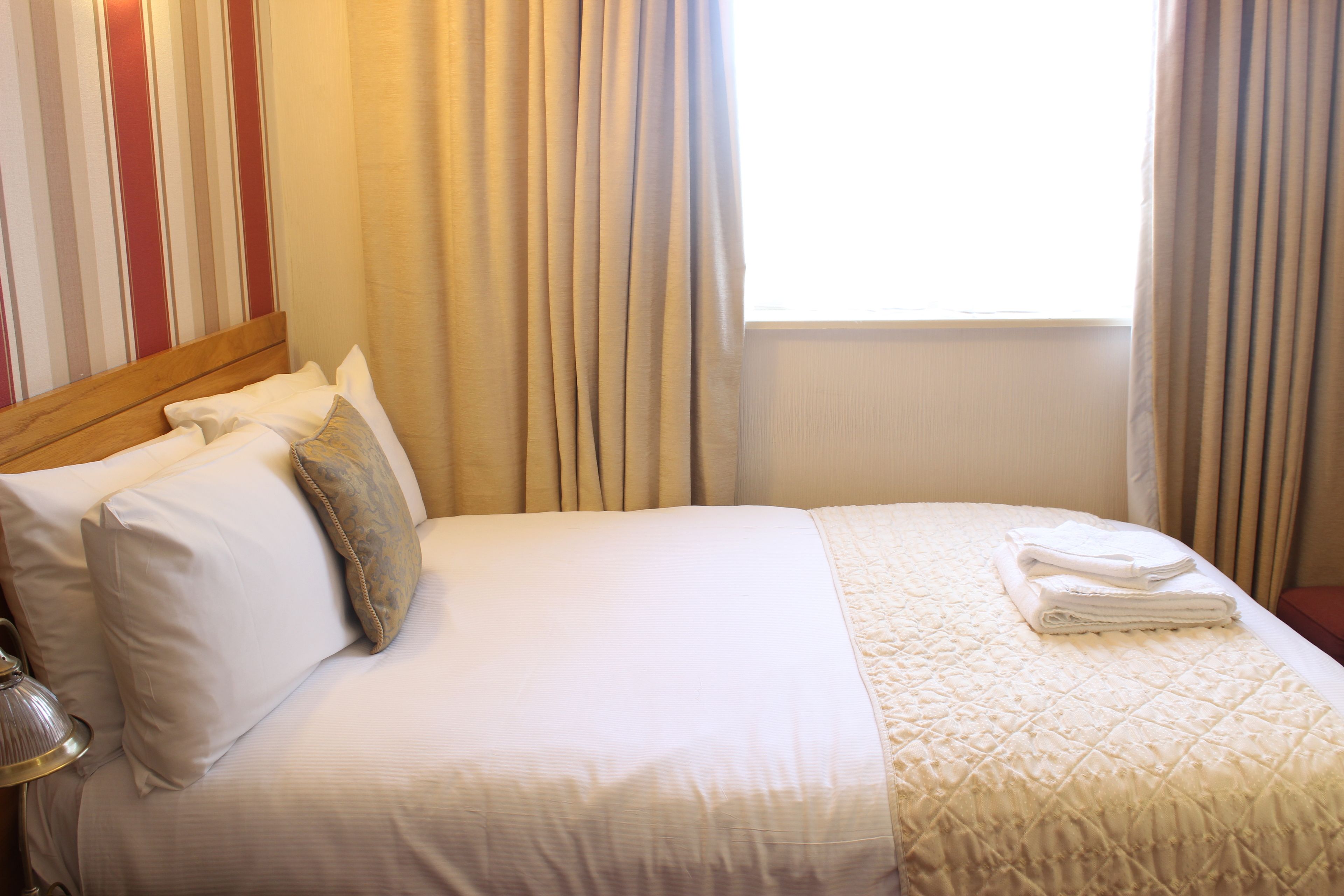 A neatly made bed with white linens, a wooden headboard, and a window with curtains.