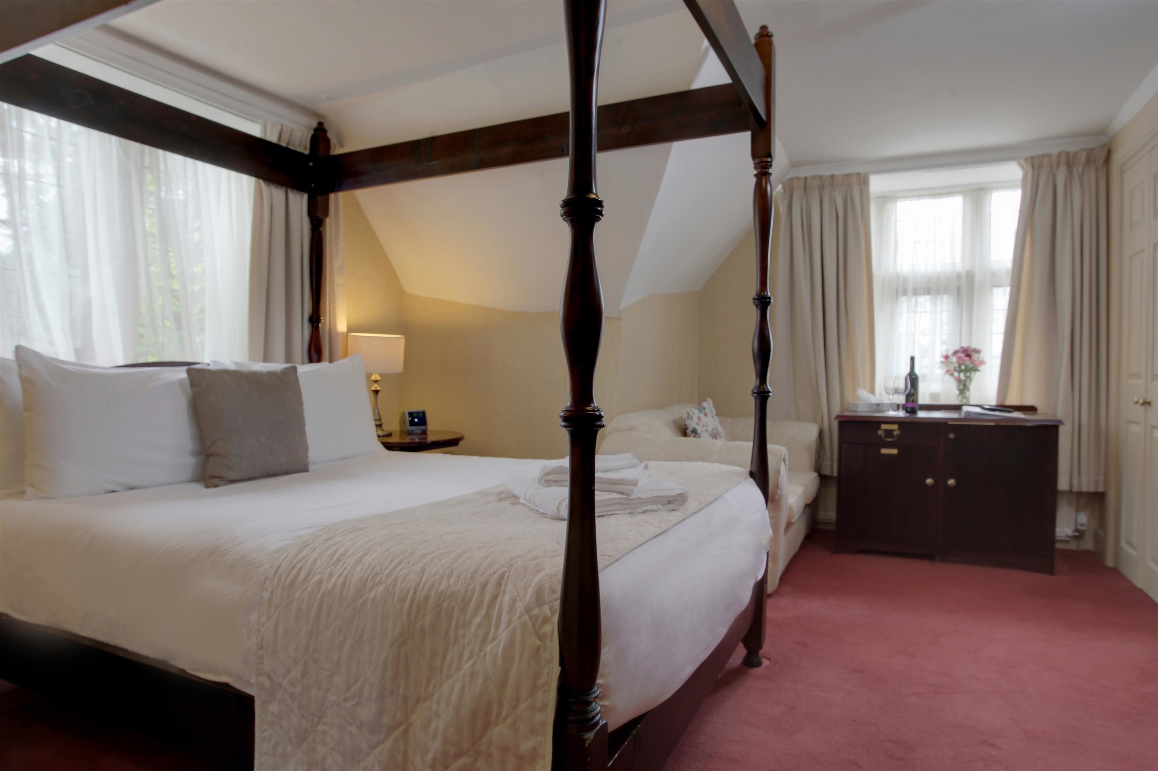 A four-poster bed with a wooden frame, a bedside table with a lamp, and a dresser with a mirror.