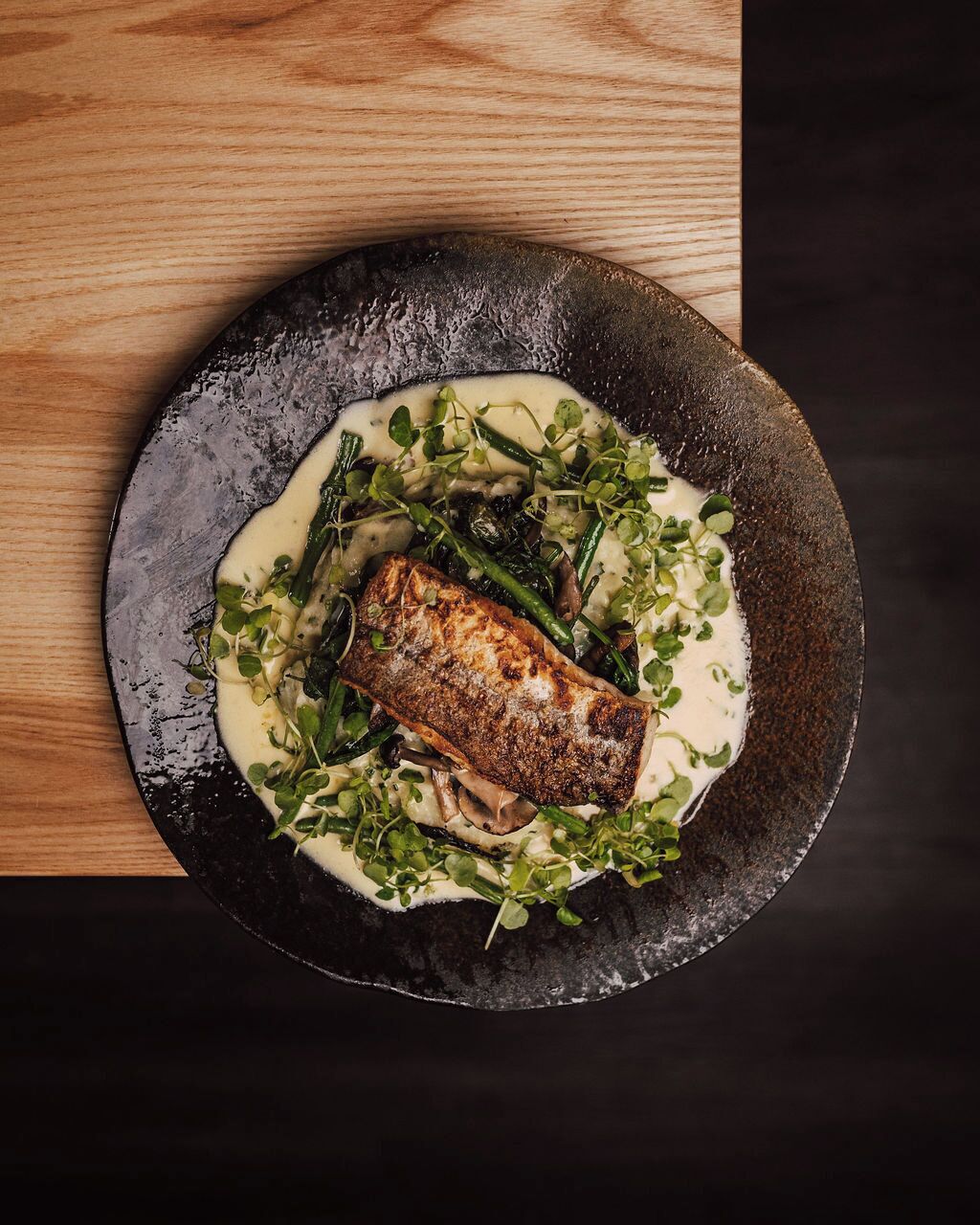 A plate of food with a piece of fish, greens, and mushrooms.