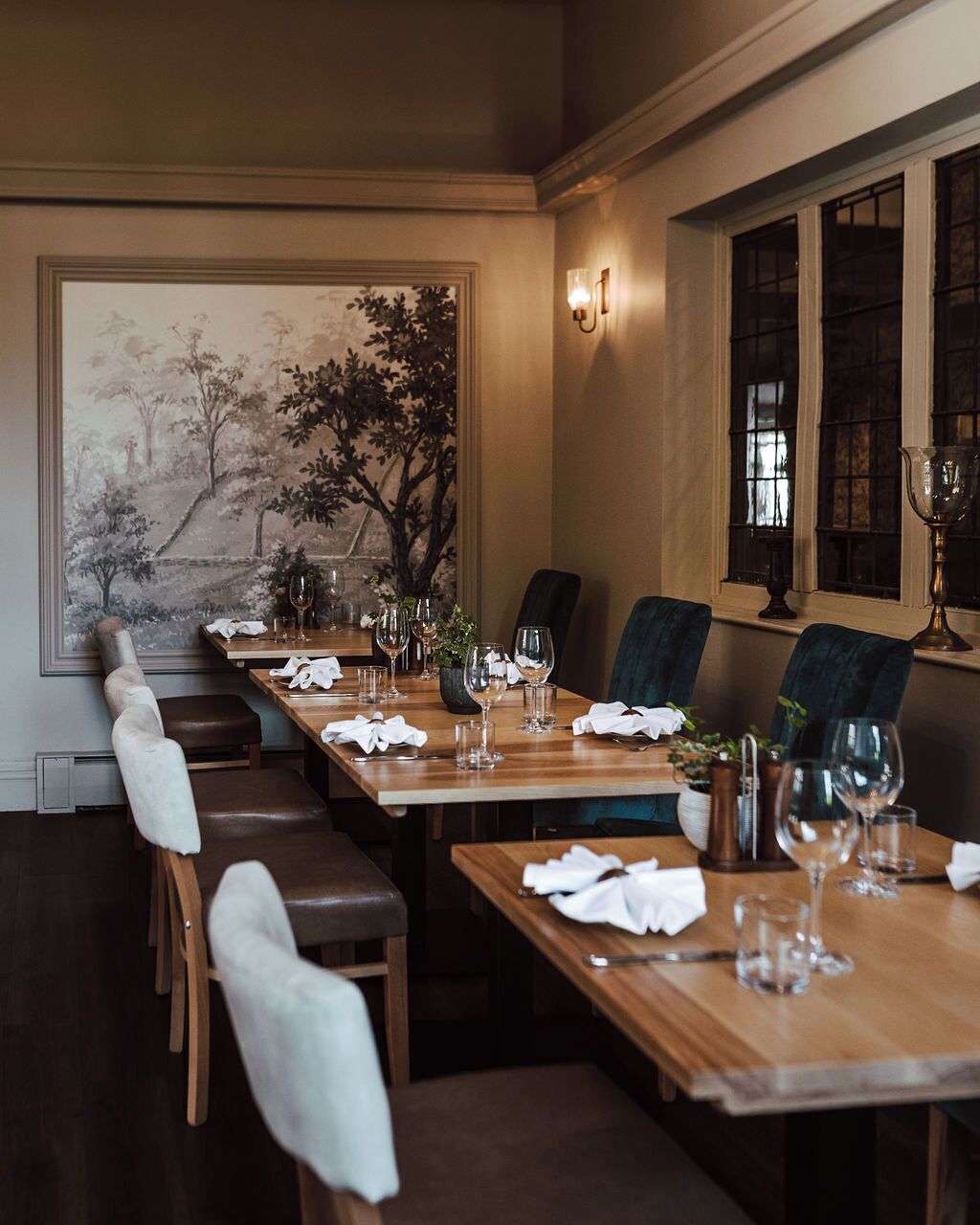 A dining area with a long table set for a meal, chairs, a vase with flowers, and a painting on the wall.