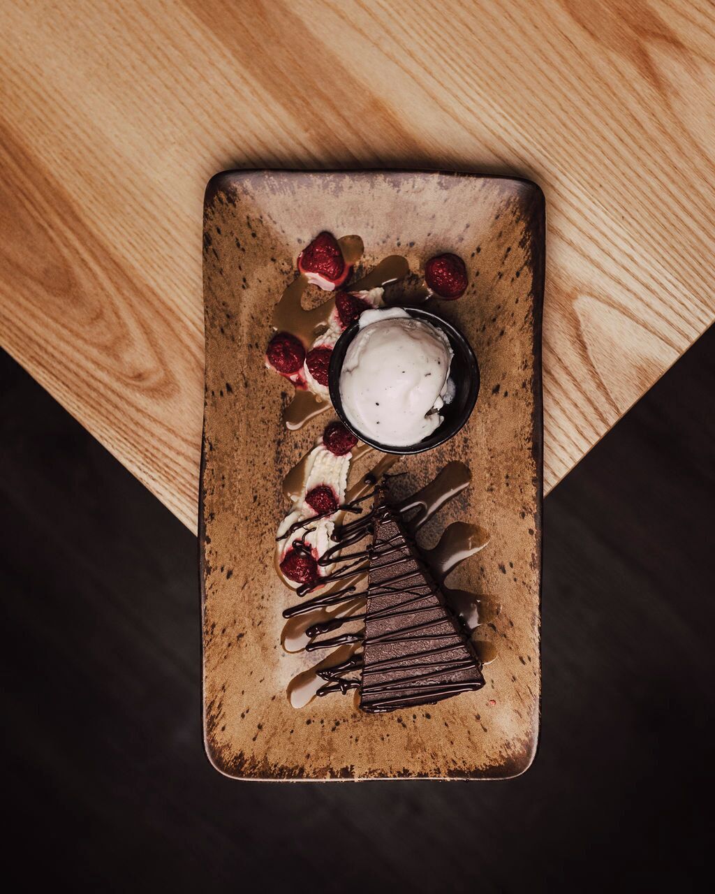 Un postre en un plato rústico de cerámica con trozos de chocolate y una bola de helado.