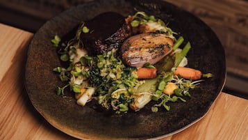 A plate of food with a variety of vegetables and a piece of meat on a dark plate, placed on a wooden table.