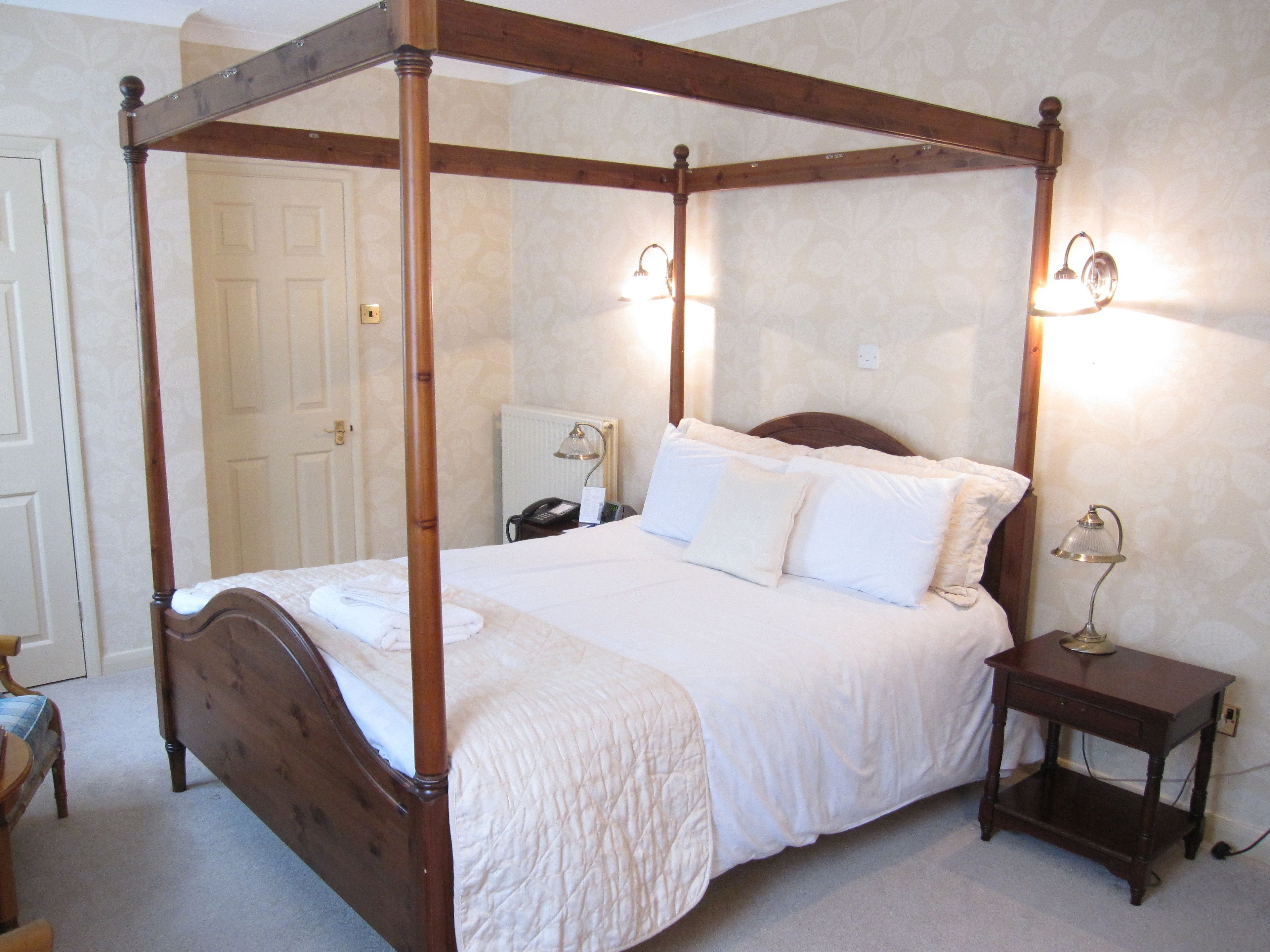 A four-poster bed with white bedding, a bedside table with a lamp, and a nightstand with a phone.