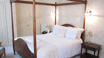A four-poster bed with white bedding, a bedside table with a lamp, and a nightstand with a phone.