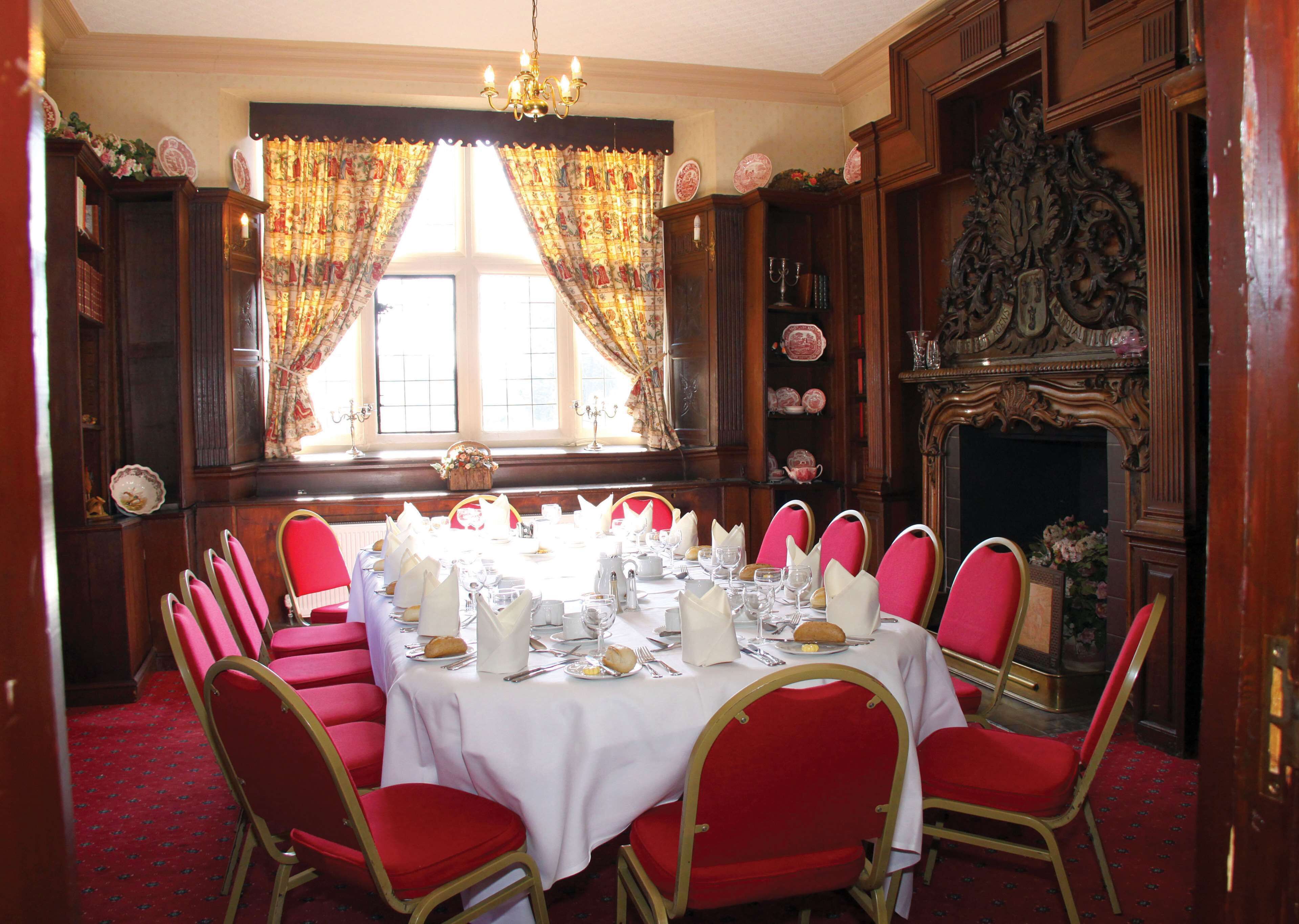 A formal dining room with a long table set for a meal, red chairs, and a fireplace.