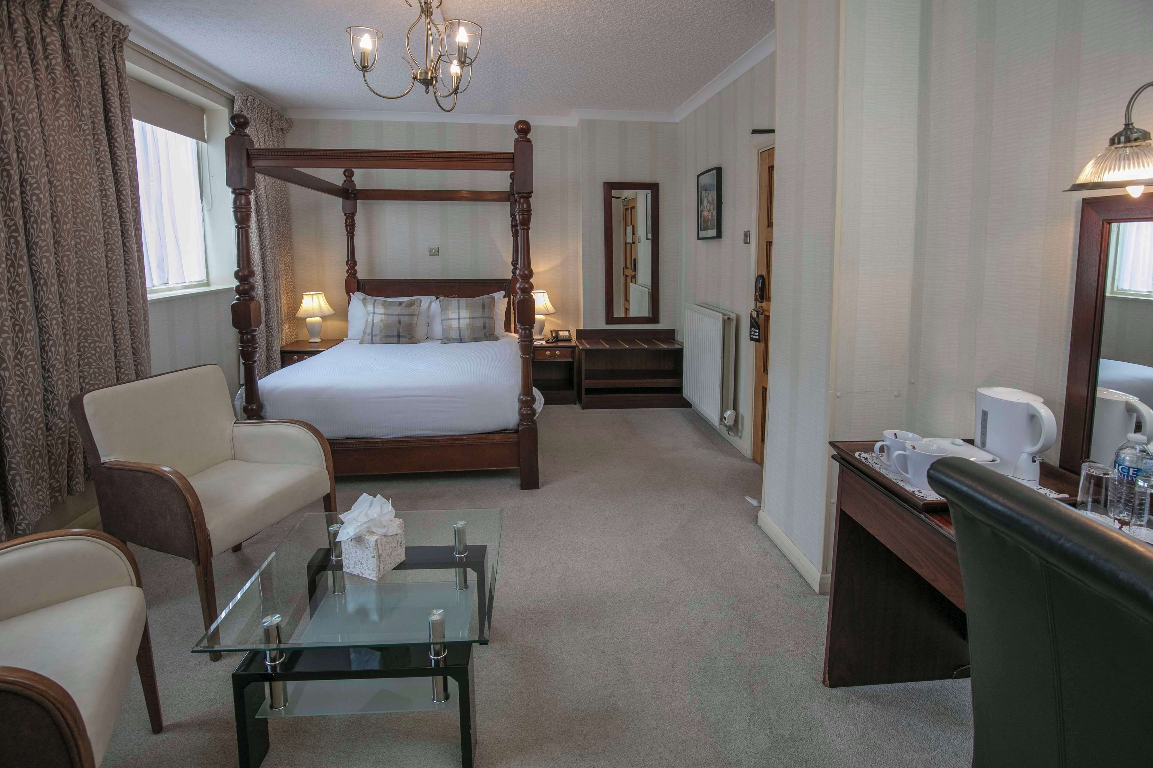 A four-poster bed with a nightstand, a glass coffee table, a desk with a chair, and a mirror.