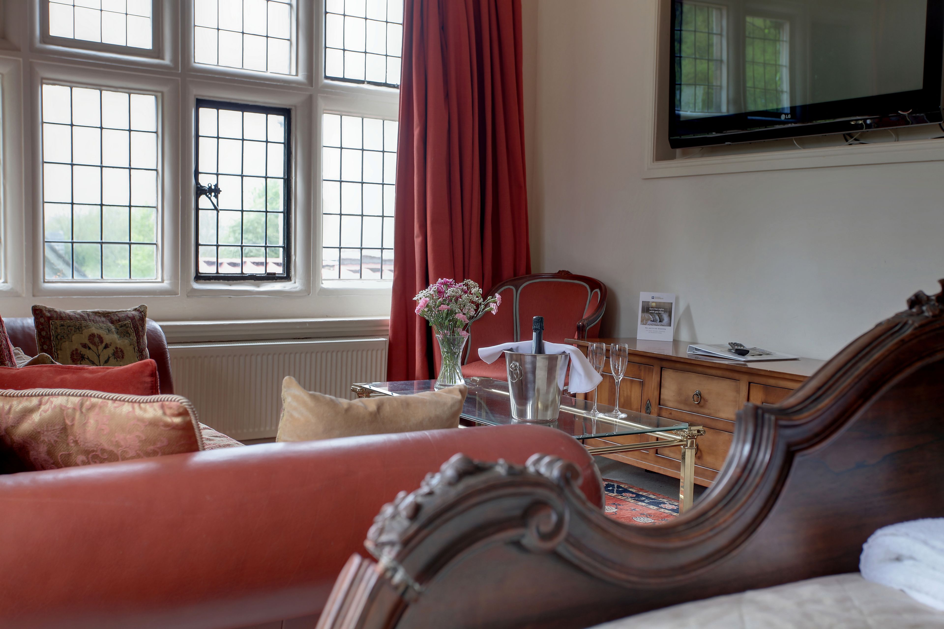 A living room with a red sofa, a wooden cabinet, a glass table, and a TV mounted on the wall.