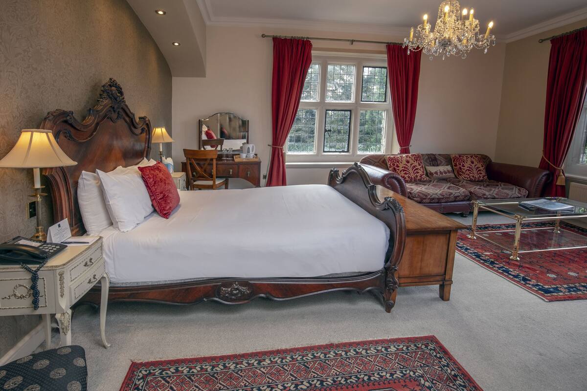 Une chambre spacieuse avec un grand lit, une table de chevet en bois, un bureau avec une chaise, un canapé et un lustre.