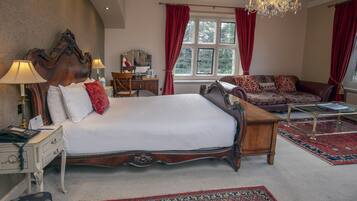 Een ruime slaapkamer met een groot bed, een houten nachtkastje, een bureau met stoel, een bank en een kroonluchter.