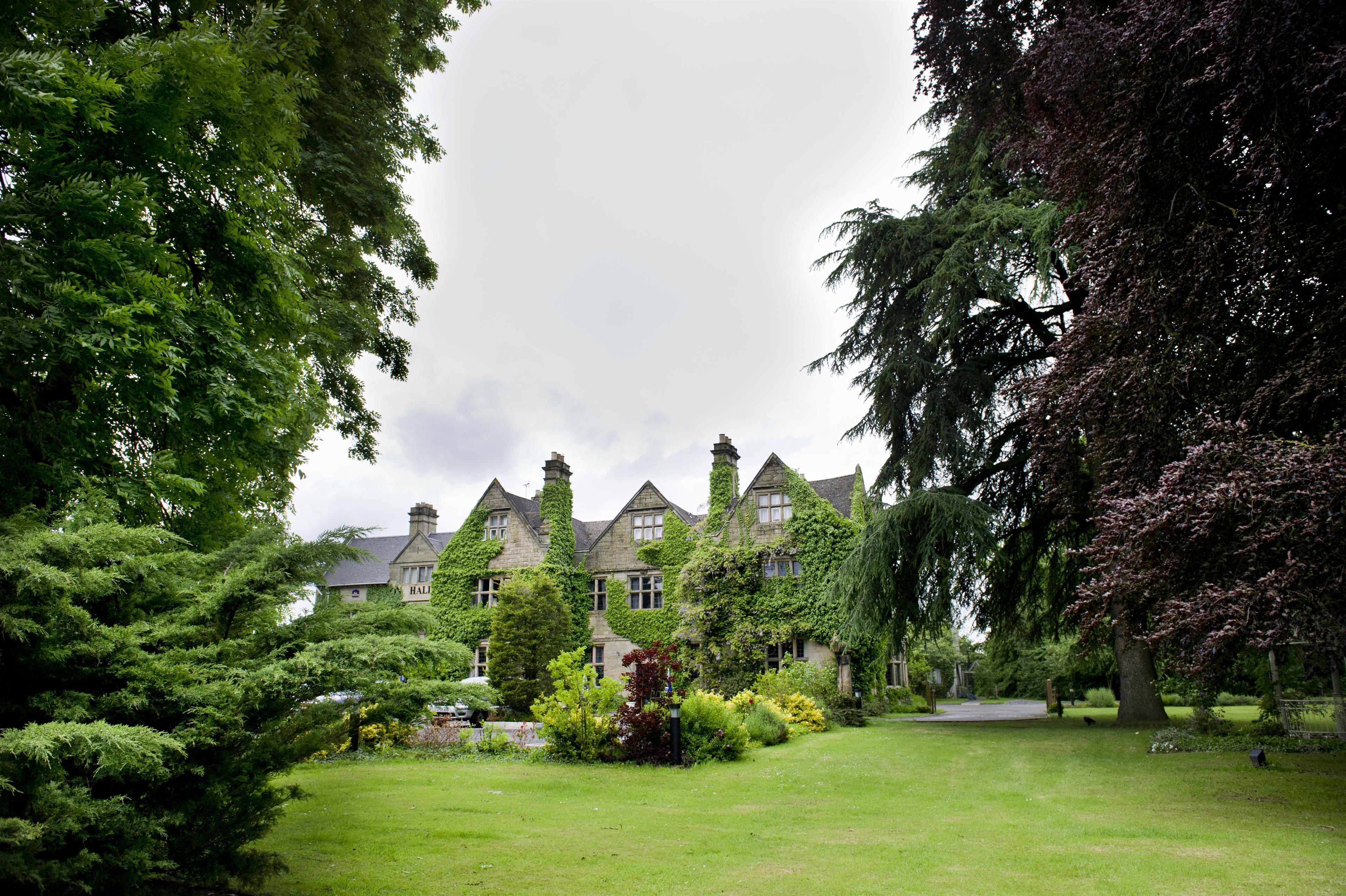 A large, ivy-covered building with multiple chimneys, surrounded by lush greenery and a well-maintained lawn.