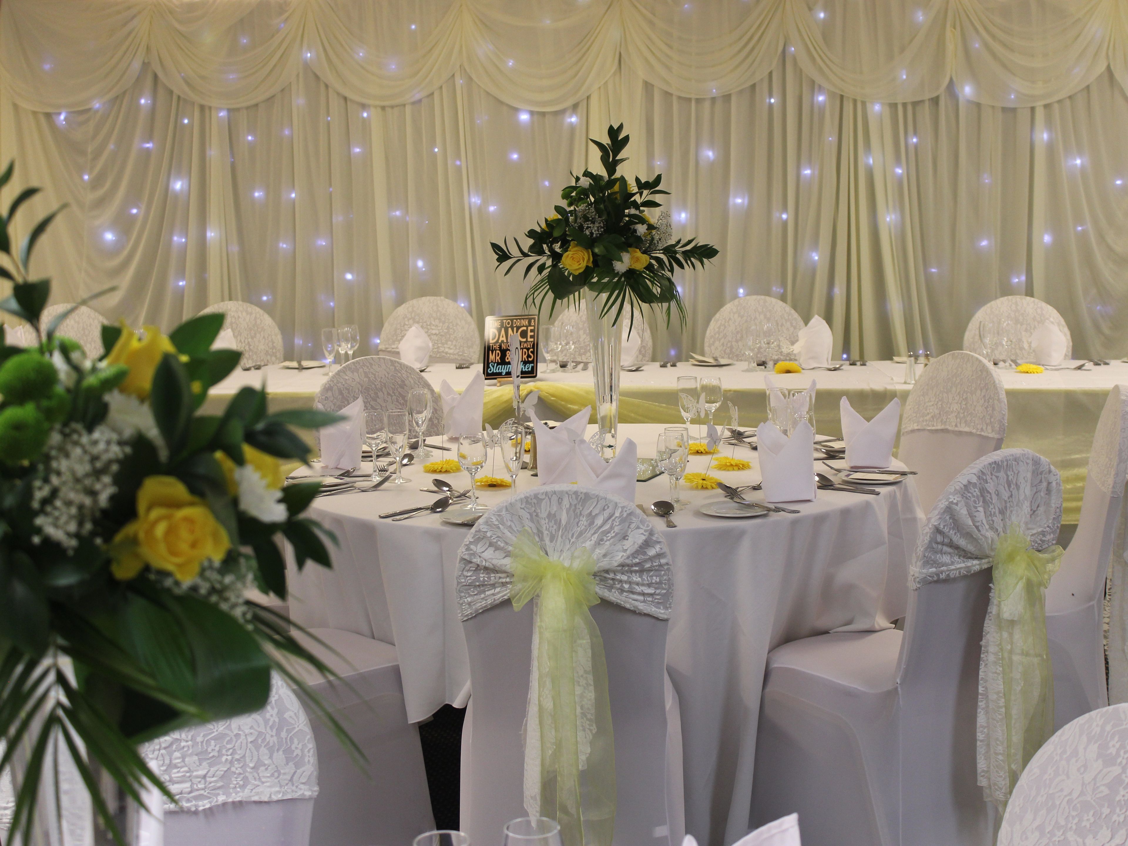 A banquet hall with round tables set for a formal event, complete with white tablecloths, glassware, and floral centerpieces.