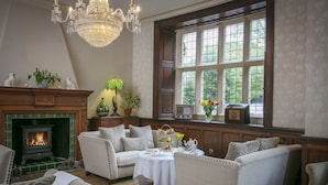 A cozy room with a fireplace, comfortable seating, a table with a tray of snacks, and a large window with a view of greenery. - Weston Hall Hotel, Sure Hotel Collection by Best Western (Bedworth)