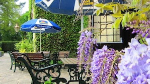 An outdoor seating area with tables and benches, surrounded by lush greenery and purple flowers. - Weston Hall Hotel, Sure Hotel Collection by Best Western (Bedworth)