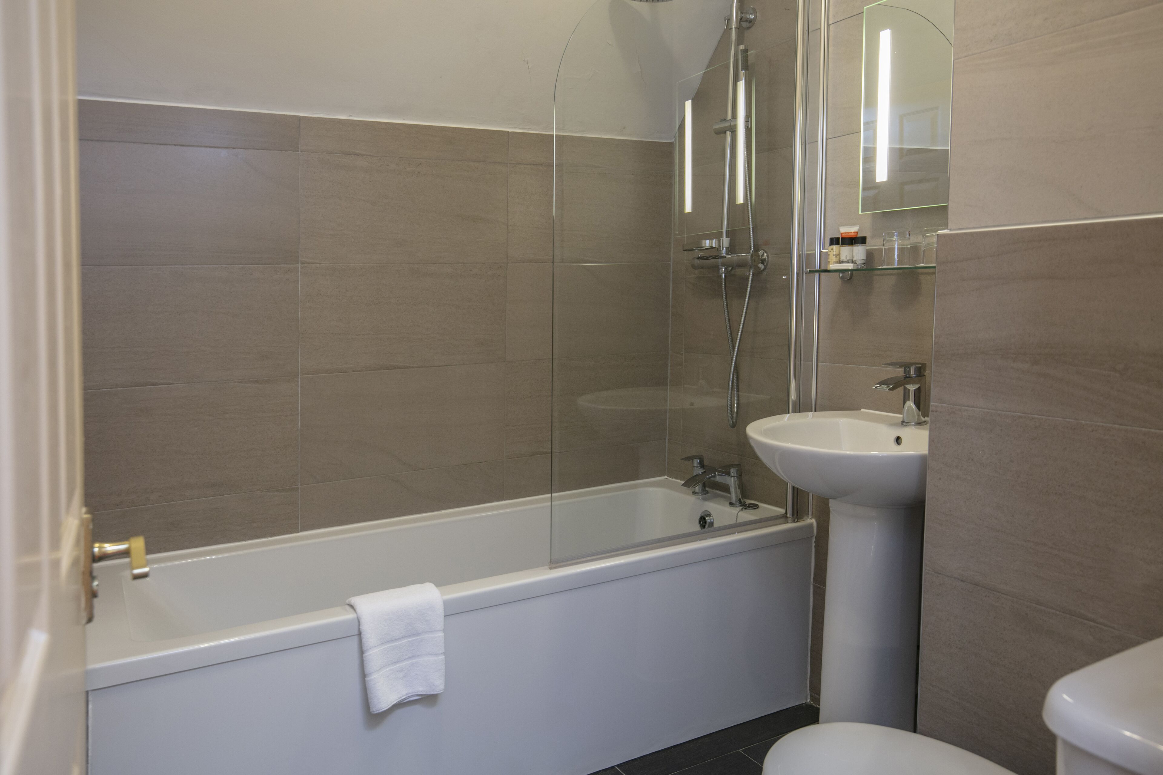 A modern bathroom with a glass-enclosed shower, a white bathtub, and a pedestal sink.