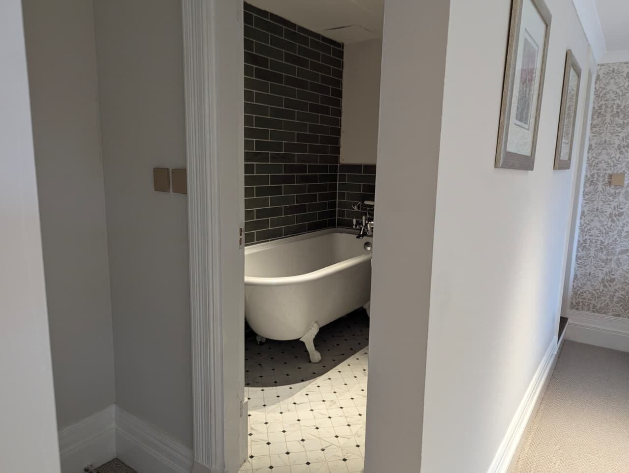 Un baño con bañera independiente, paredes de azulejos oscuros y piso estampado.