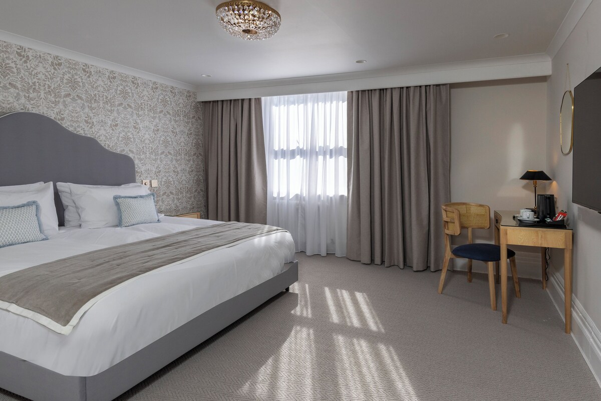 A hotel room with a large bed, a desk, a chair, and a window with curtains.