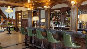 Zona de bar con taburetes de madera, una barra y una variedad de botellas.