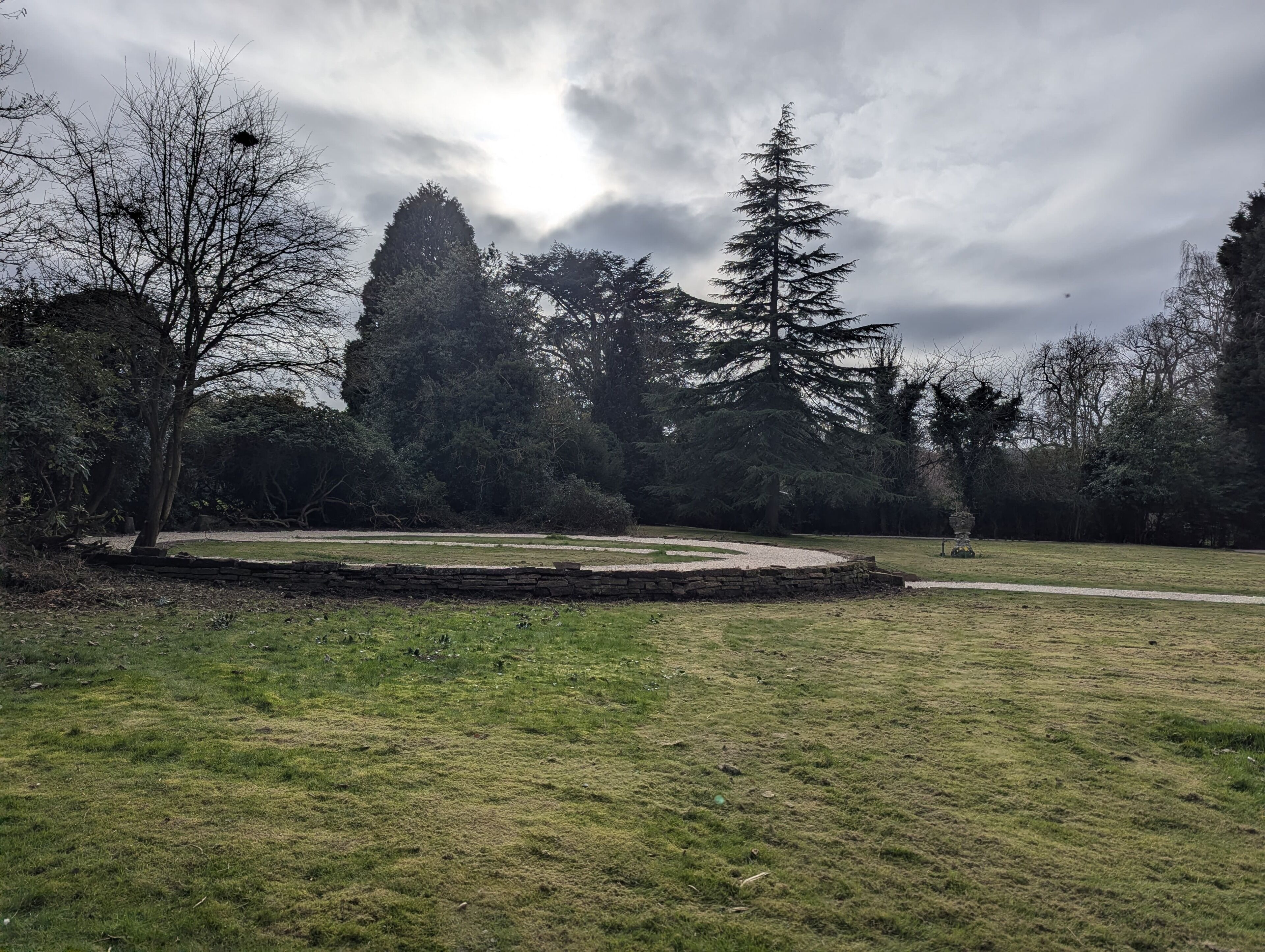 A park with a stone wall, trees, and a grassy area.