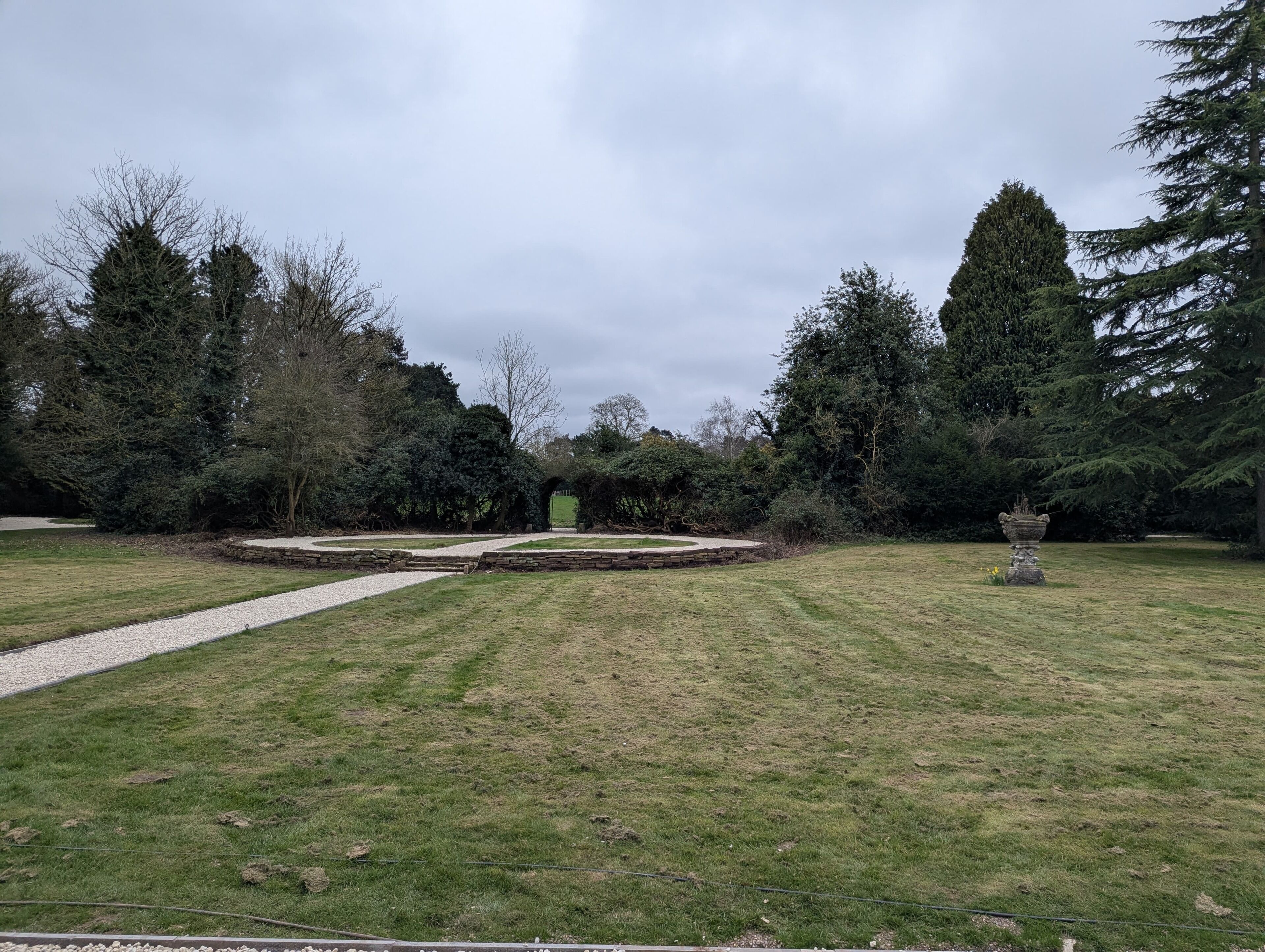 Un giardino con vialetto in ghiaia, muro in pietra e una statua.