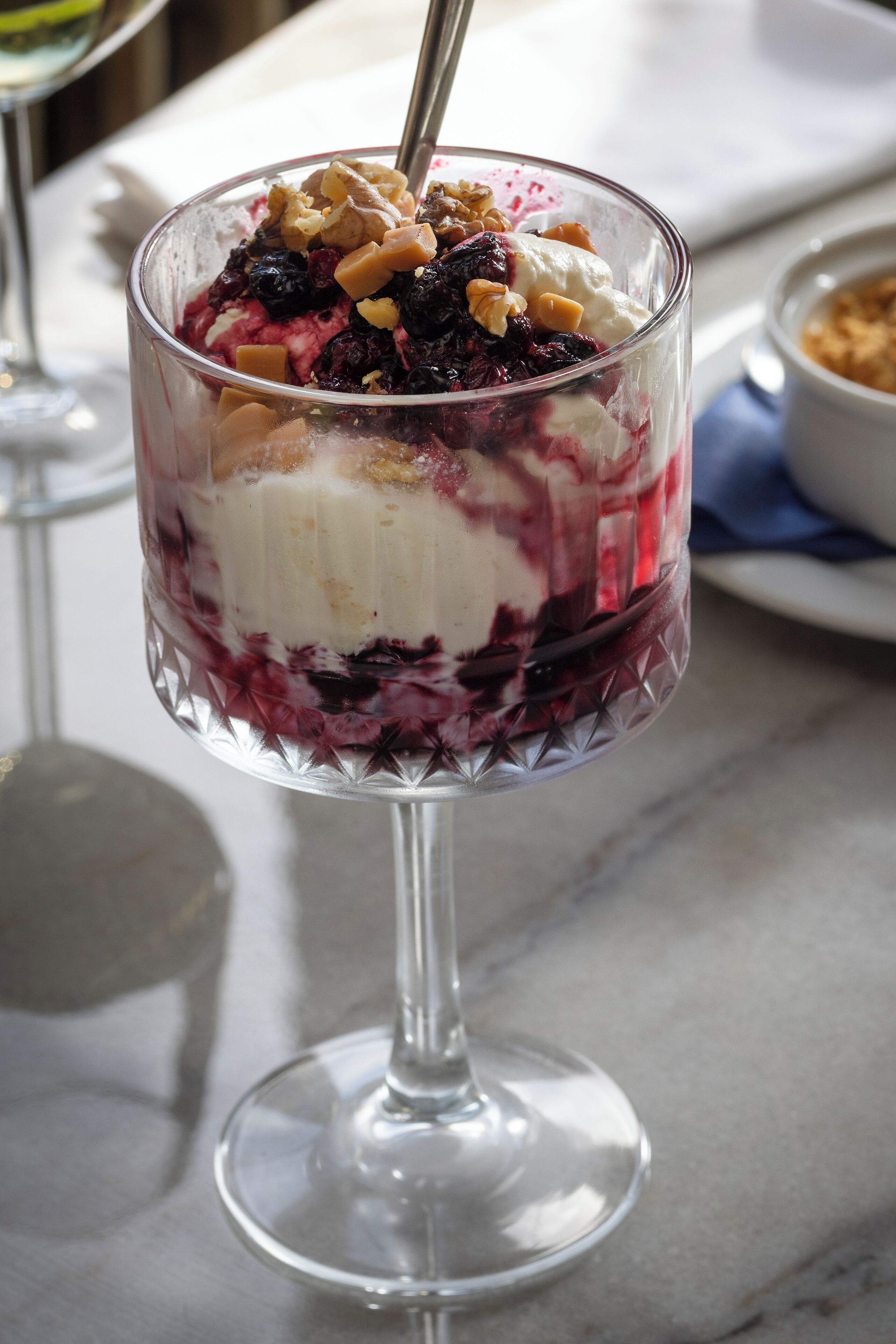 A dessert in a glass bowl with a spoon, placed on a table.