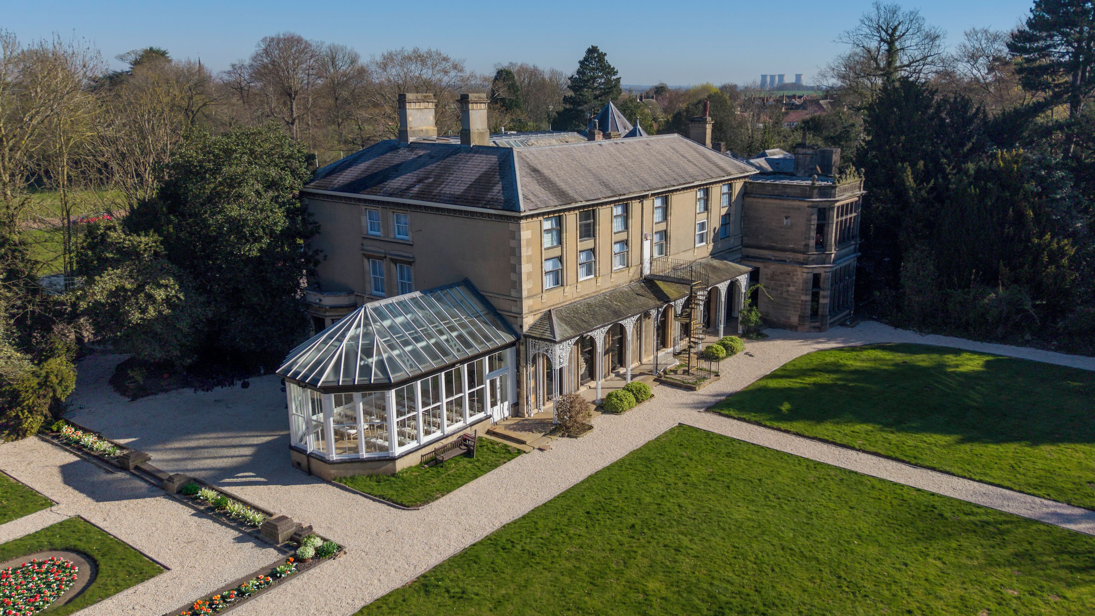 A large, historic building with a conservatory, a well-manicured lawn, and a gravel driveway.