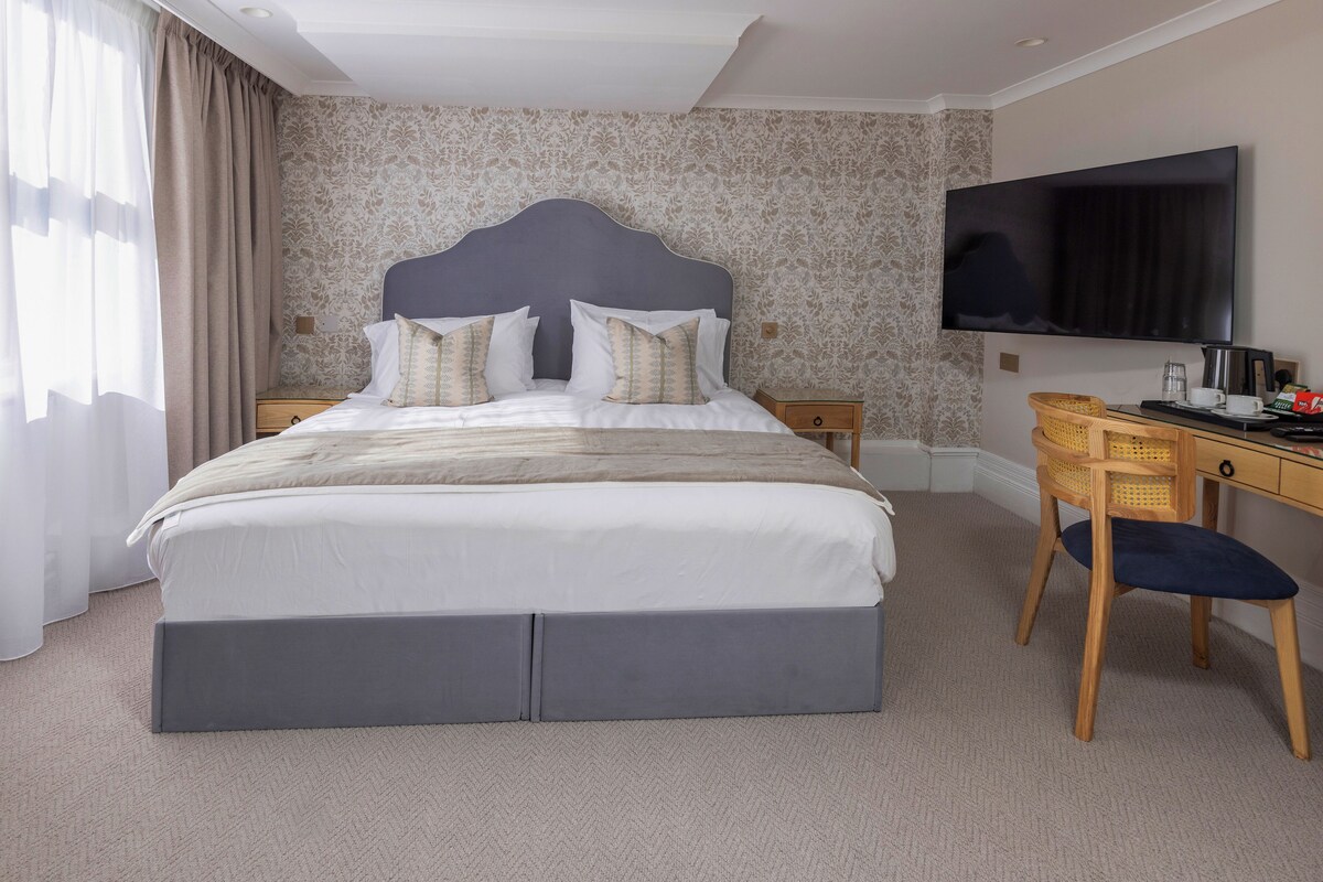 A hotel room with a bed, a desk, a chair, a television, and a wall-mounted TV.